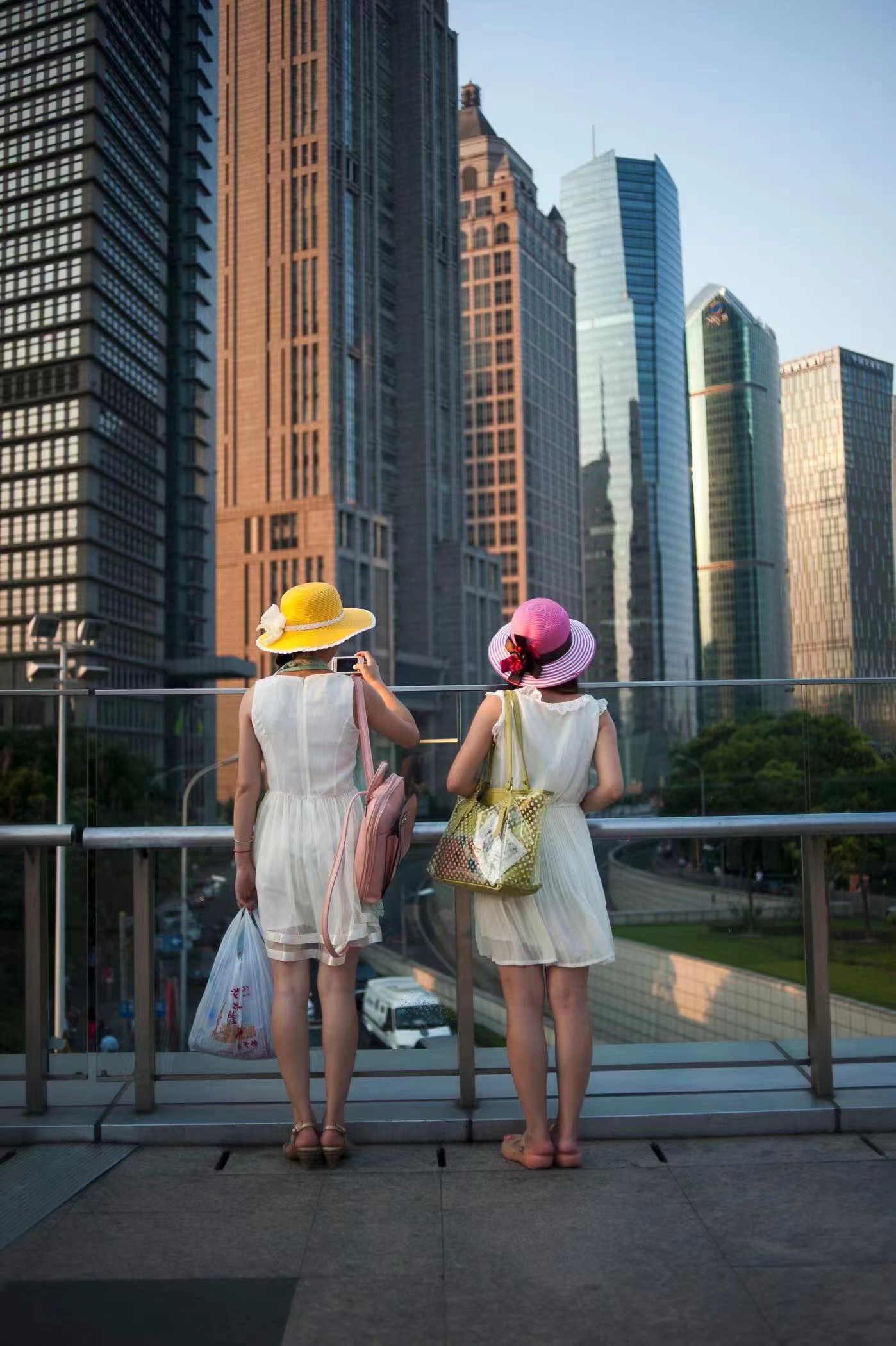 2013年7月11日，中国上海，两名年轻女性游客欣赏着世纪大道上天桥周围的天际线。浦东的天际线已经成为主要的旅游吸引卡，也是中国成为全球经济强国的象征。