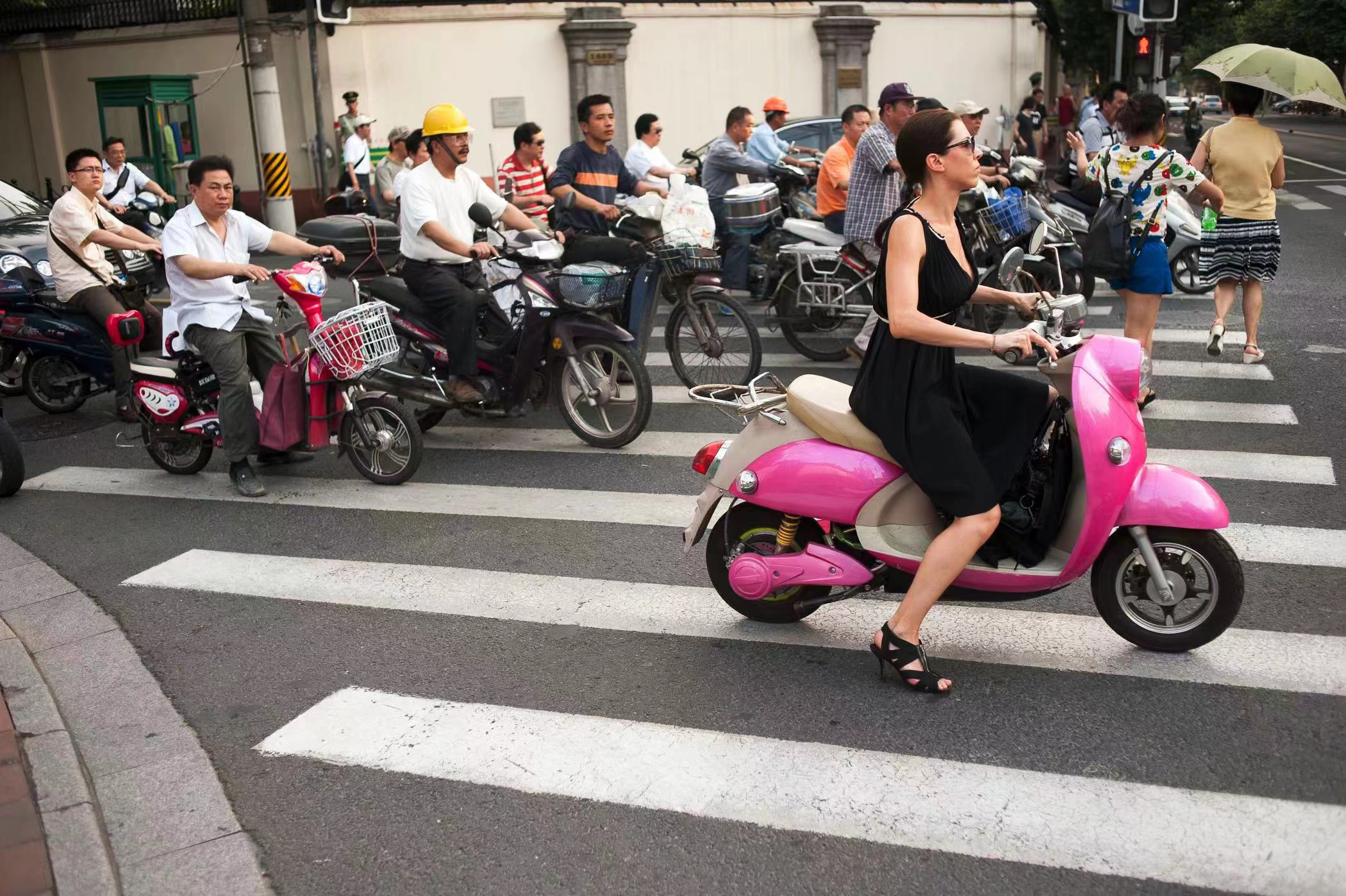 2013年7月2日，中国上海，乌鲁木齐路和淮海路的交叉口，一名外籍女子骑着一辆中国制造的粉色电动助力车，等交通信号灯。